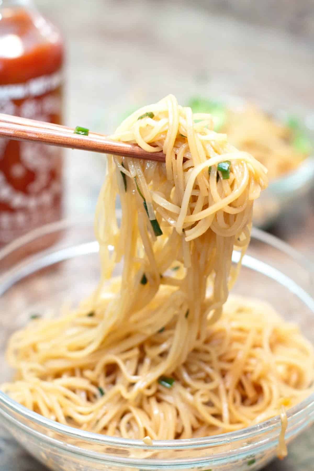 chopsticks holding up noodls over a bowl.