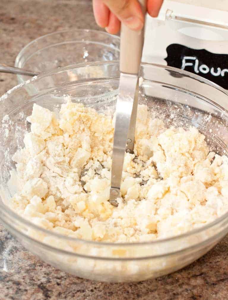 a mashed potato masher mashing potatoes in a bowl.