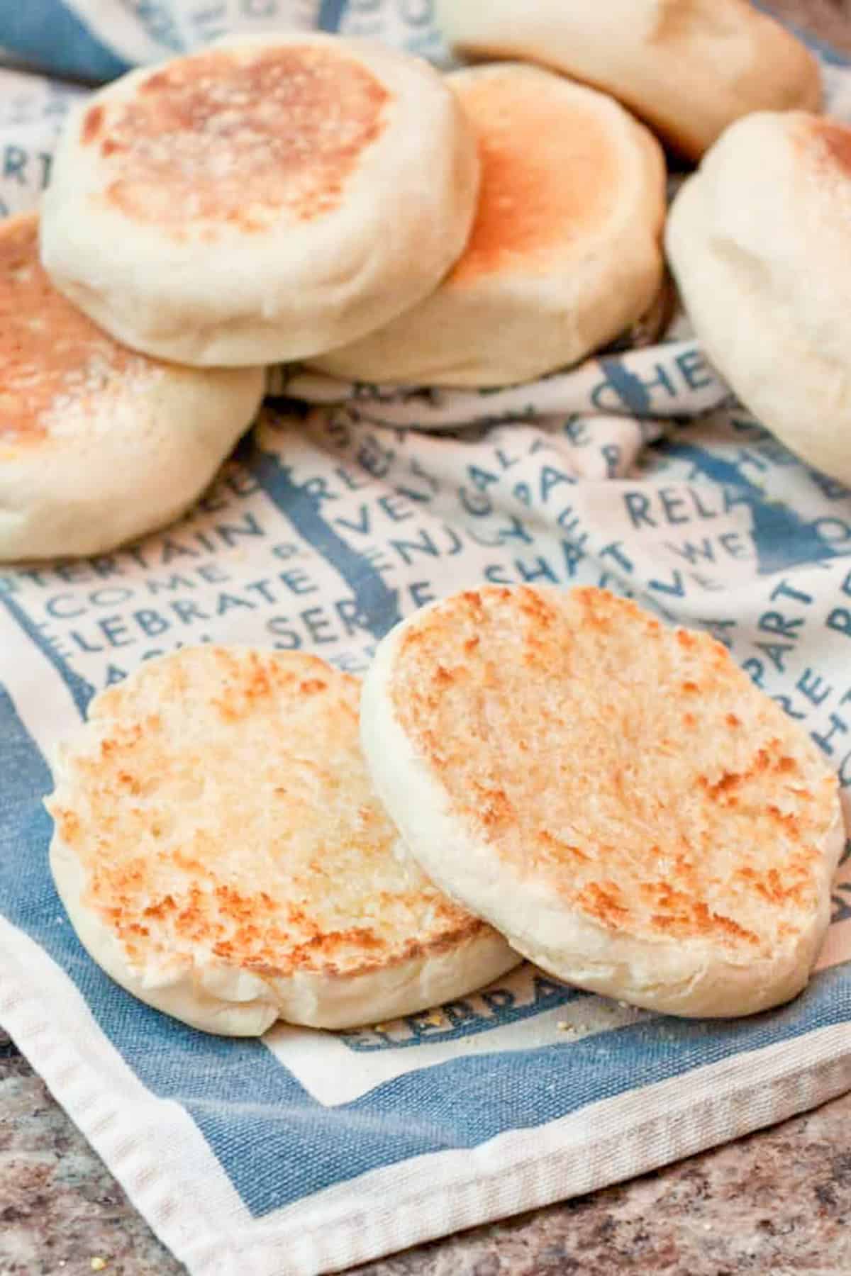 halved english muffins on a napkin with english muffins behind it.