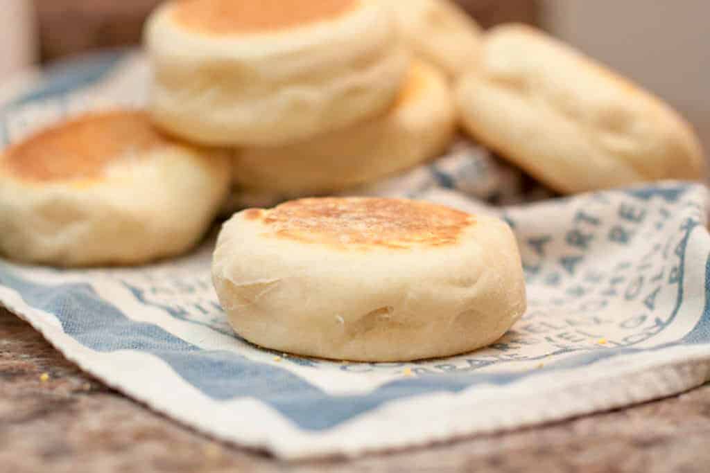 an english muffin on a tea towel with other english muffins behind it.