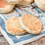 halved english muffins on a napkin with english muffins behind it.