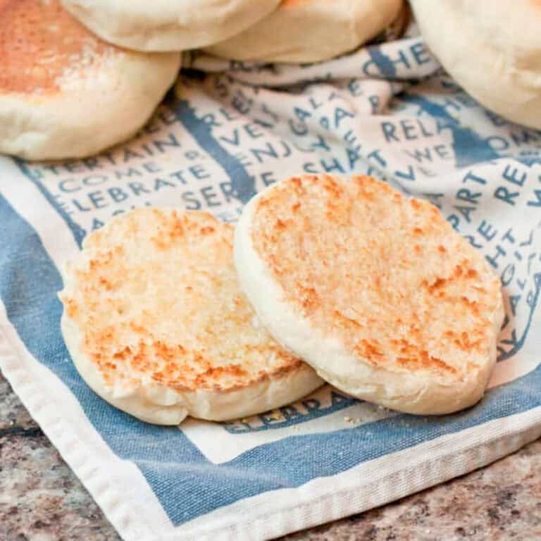 halved english muffins on a napkin with english muffins behind it.