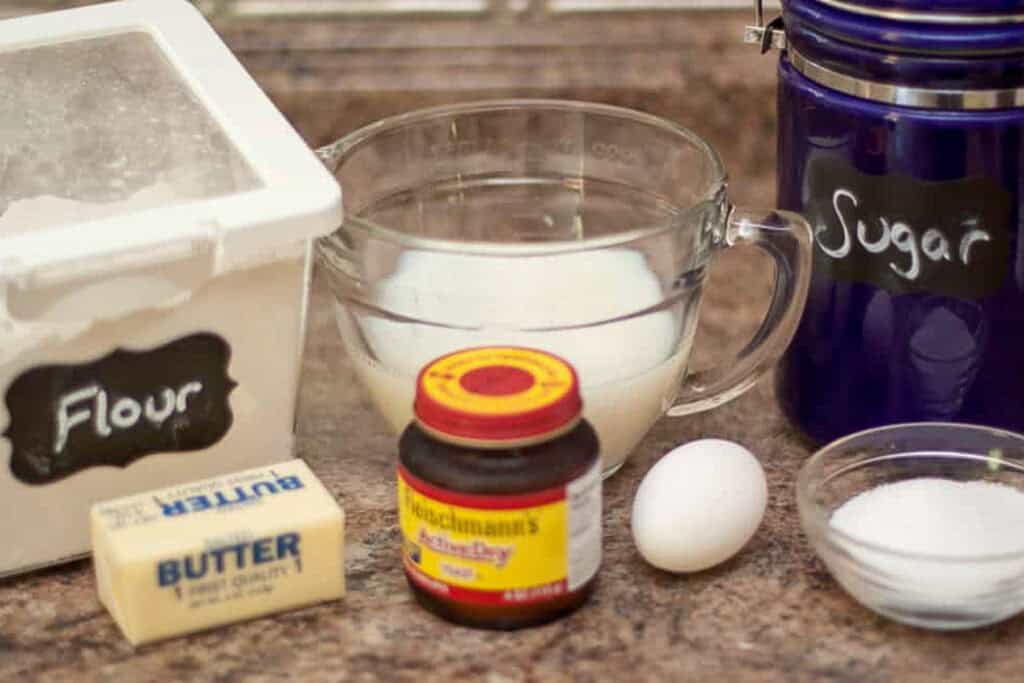 flour, milk, yeast, butter, egg, sugar, and salt on a counter.