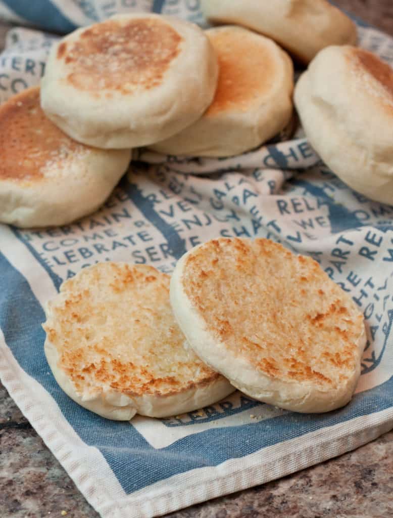 an open toasted english muffin with butter on a tea towel with muffins stacked behind