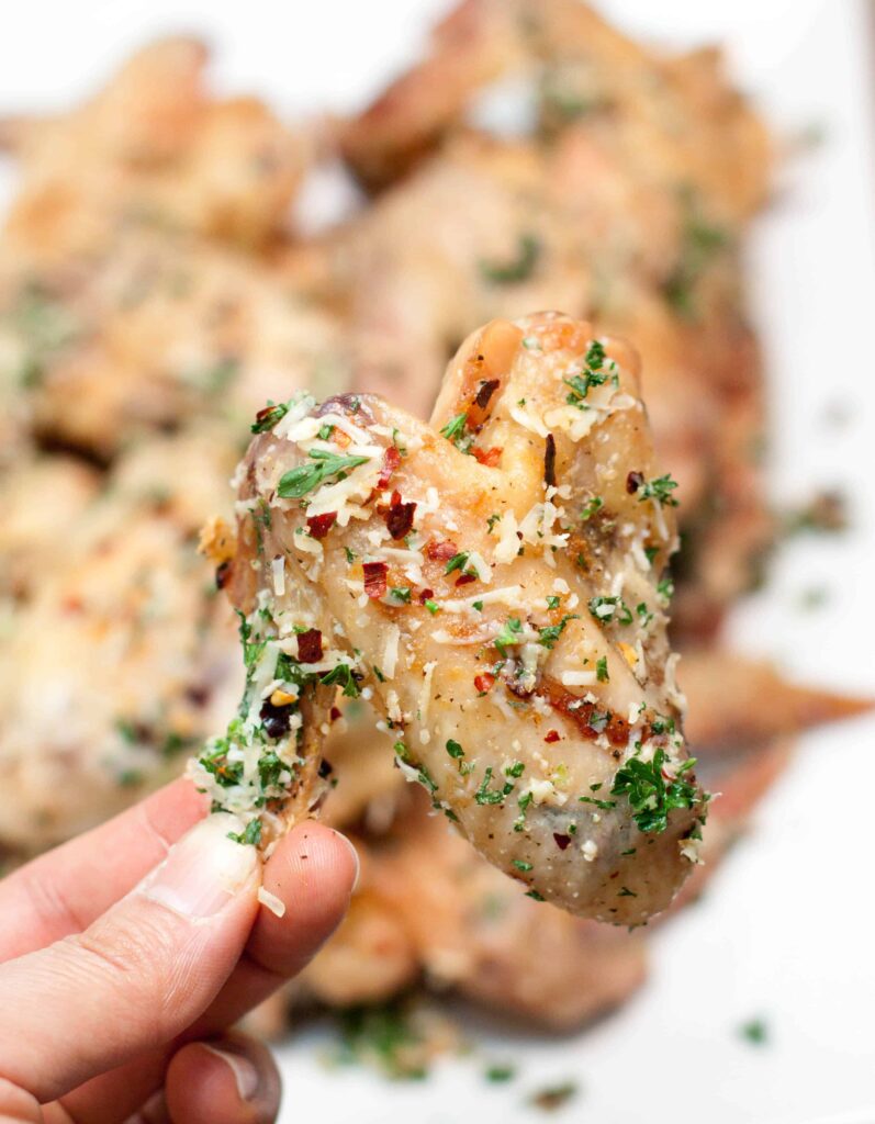 chicken wing being held up coated with cheese and parsley and red pepper flakes