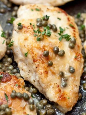 a close up of chicken in a pan topped with capers.