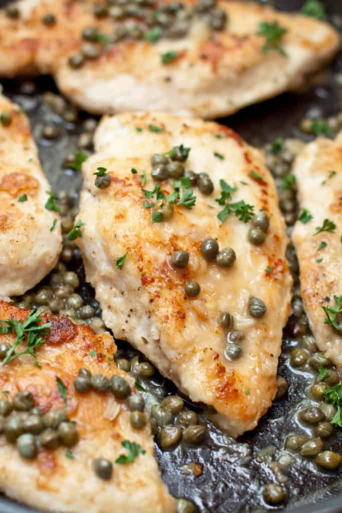 a close up of acooked chicken breasts in a pan topped with capers