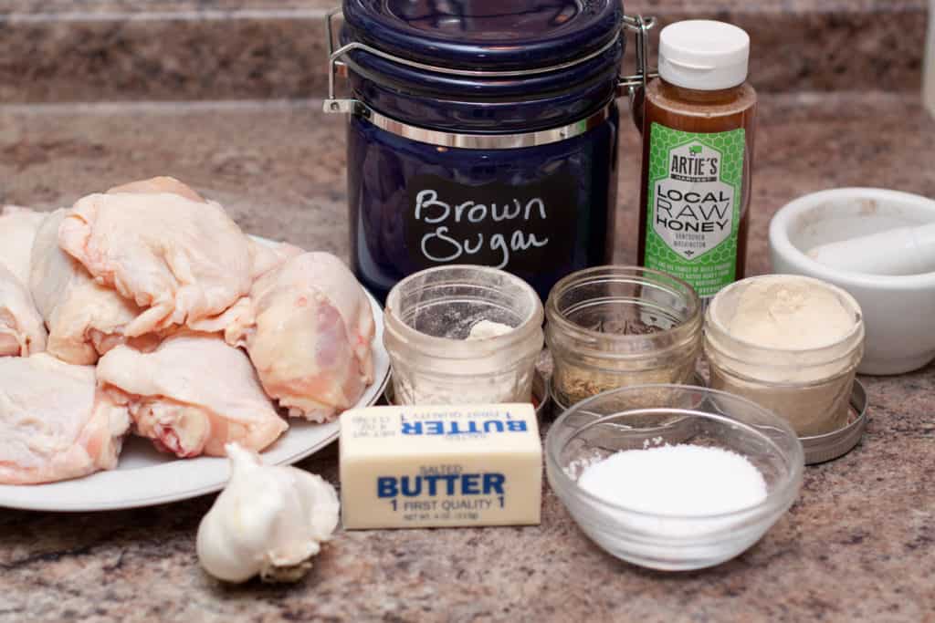 raw chicken thighs, butter, garlic, salt, spices, sugar, and honey on counter.