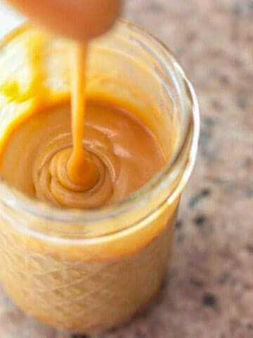 an open mason jar of caramel sauce and a spoon pouring it in.
