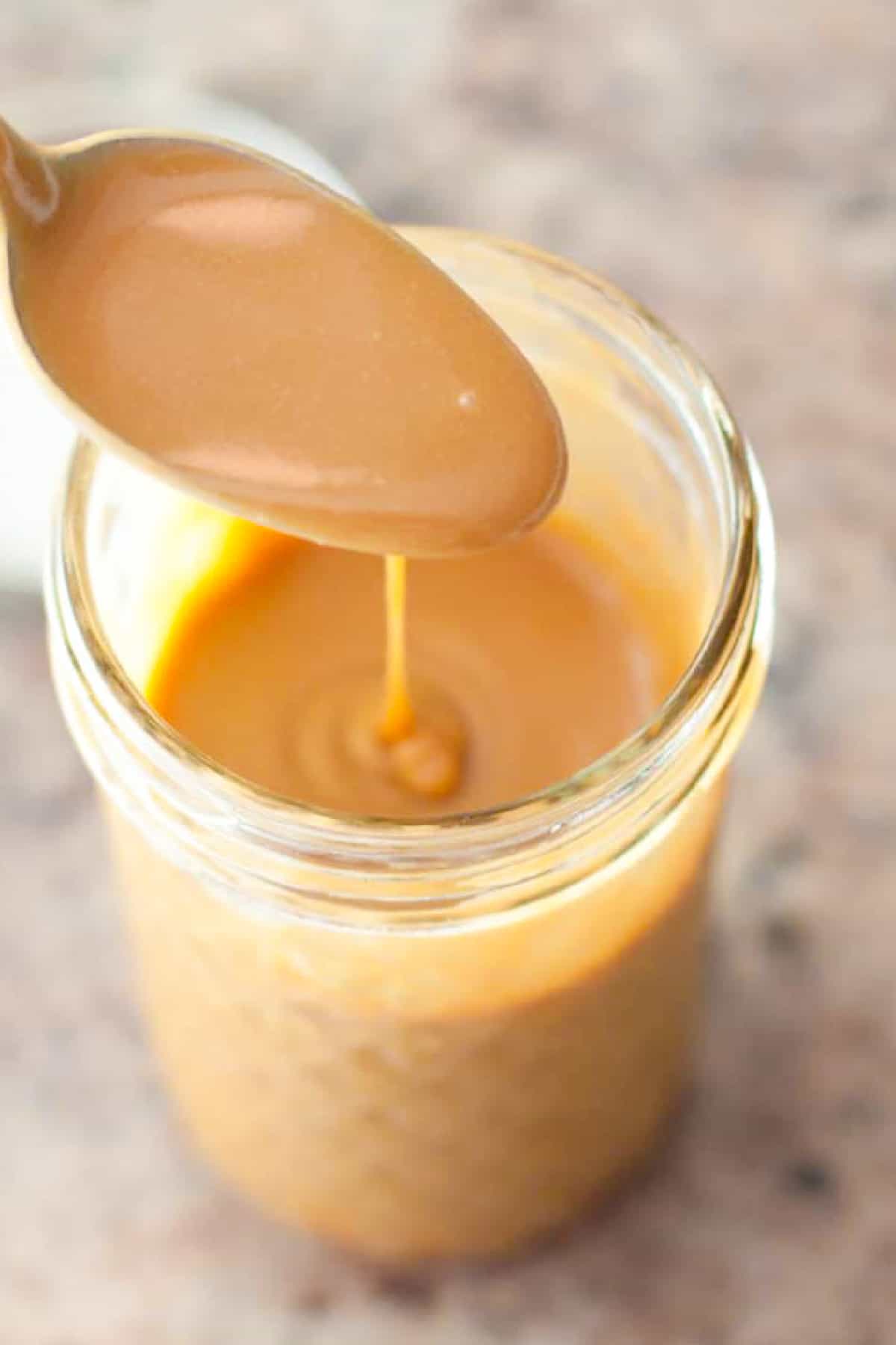 an open mason jar of caramel sauce and a spoon pouring it in.