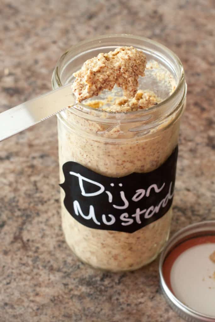 an open mason jar of mustard with a knife scooping some out.