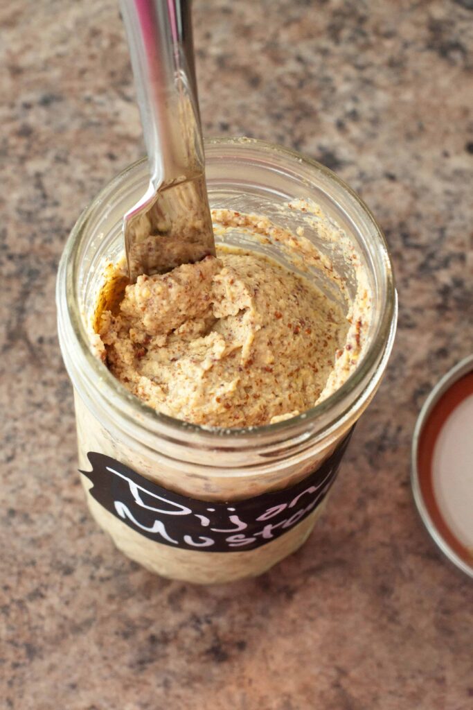 overhead of an open mason jar with dijon mustard and a knife.