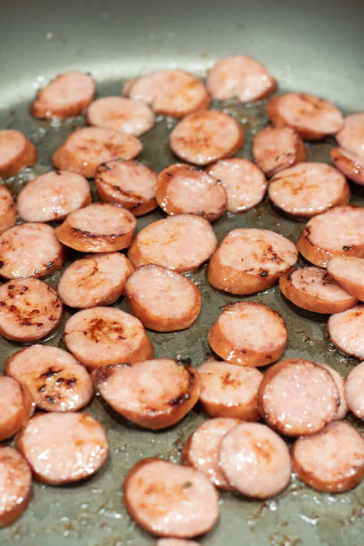 sliced kielbasa cooking in pan.