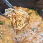 tongs holding shredded chicken in a crock pot of shredded chicken.