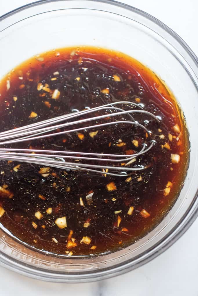 dark sauce in a bowl with garlic and a whisk.