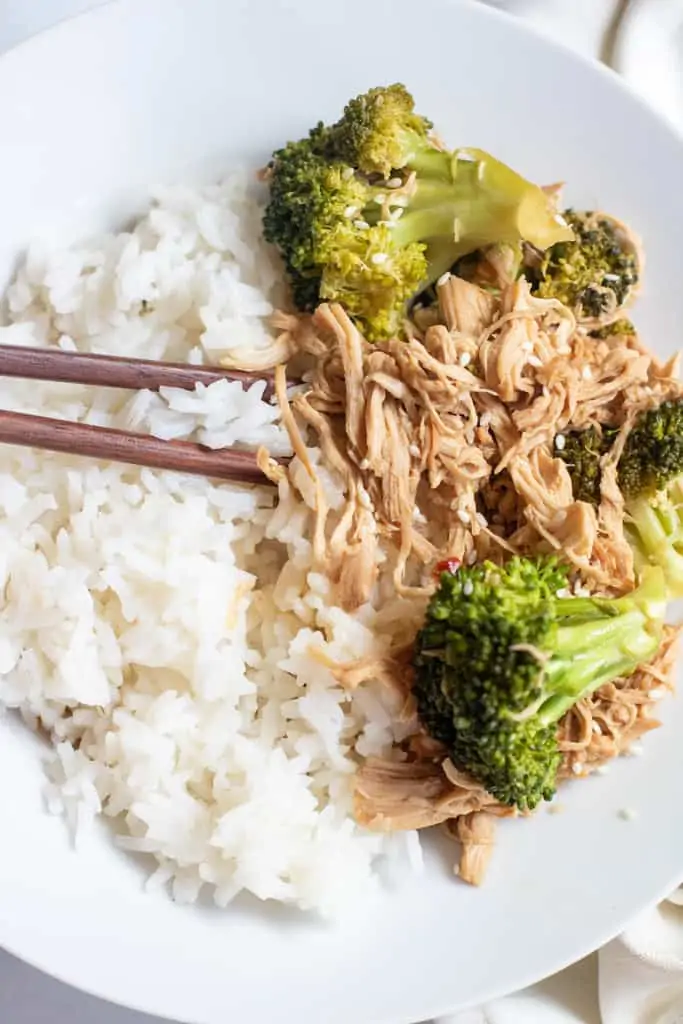 a plate with chopsticks, rice, and shredded chicken and broccoli.