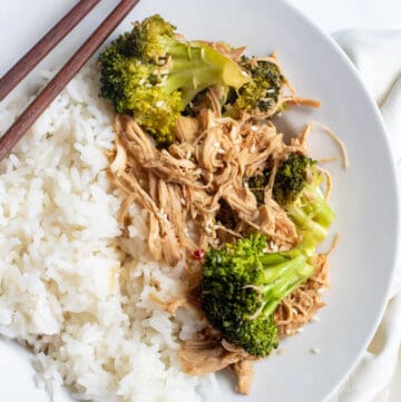 a plate with chopsticks, rice, and shredded chicken and broccoli.