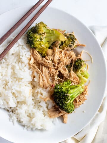 a plate with chopsticks, rice, and shredded chicken and broccoli.