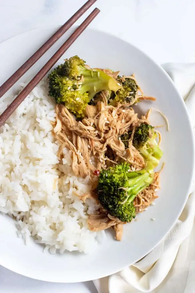 a plate with chopsticks, rice, and shredded chicken and broccoli.