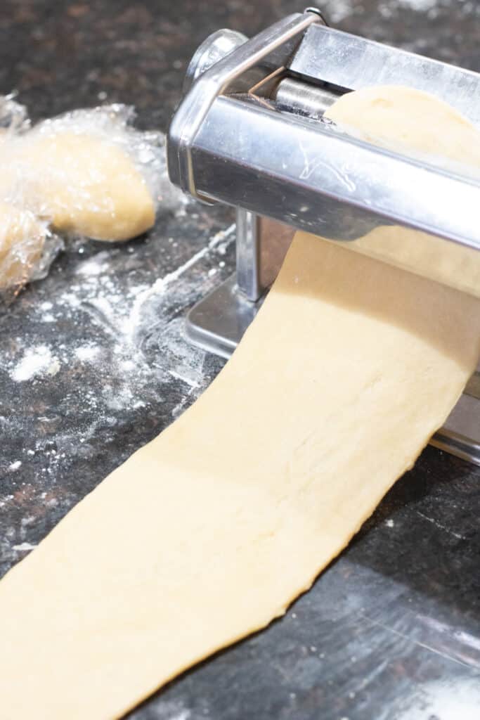 pasta dough being rolled out in a pasta roller