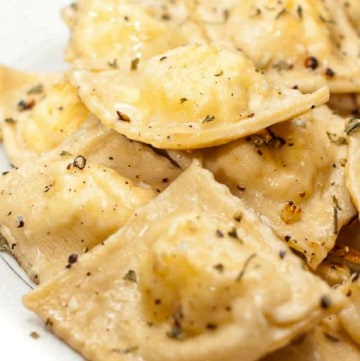 a plate of cooked ravioli with herbs and butter.