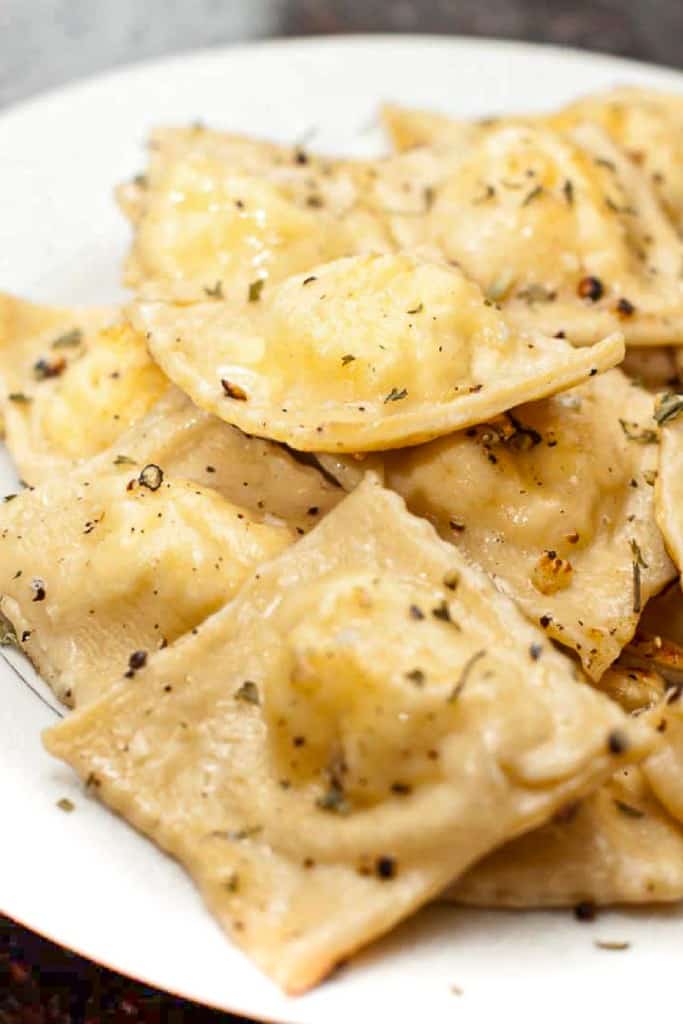 a plate of cooked ravioli with herbs and butter.