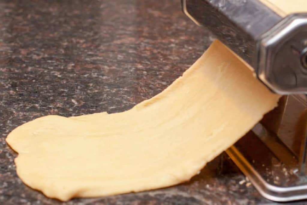 pasta dough being rolled out in a roller.