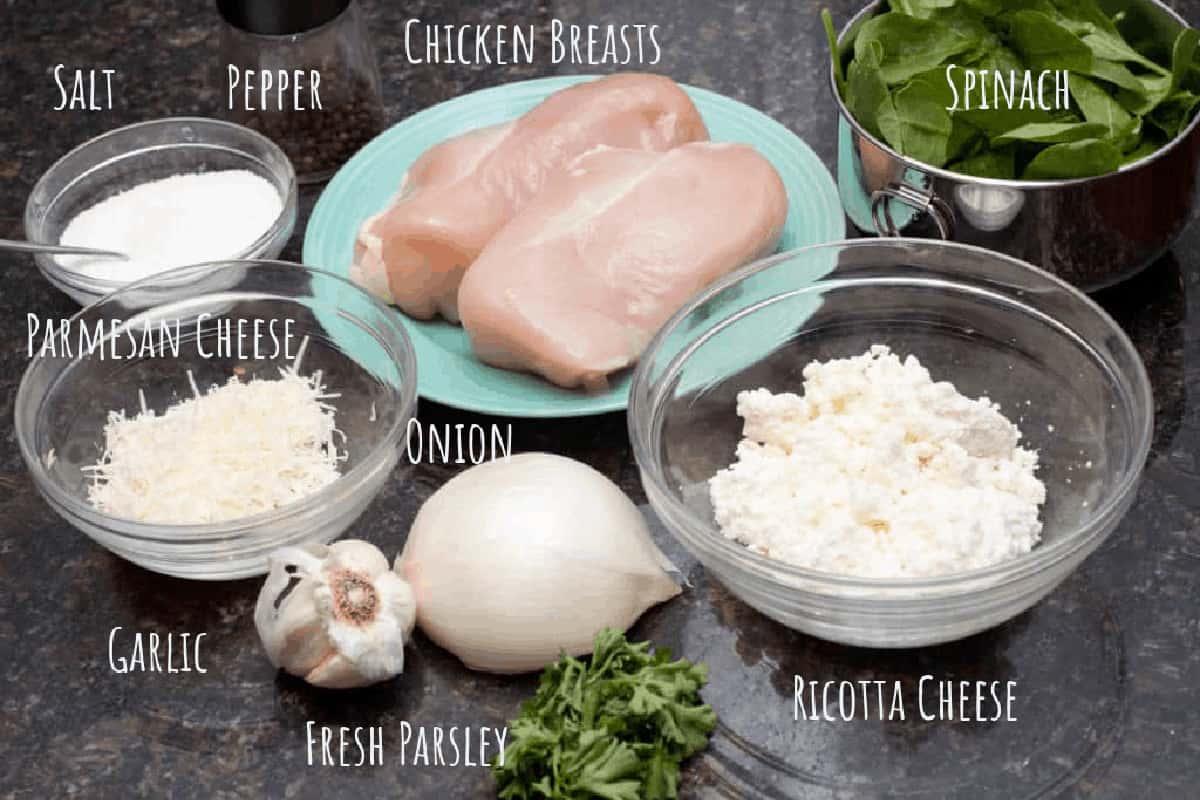 chicken breasts, spinach, ricotta cheese, parm cheese, garlic, onion, salt, pepper, and parsley on a counter.