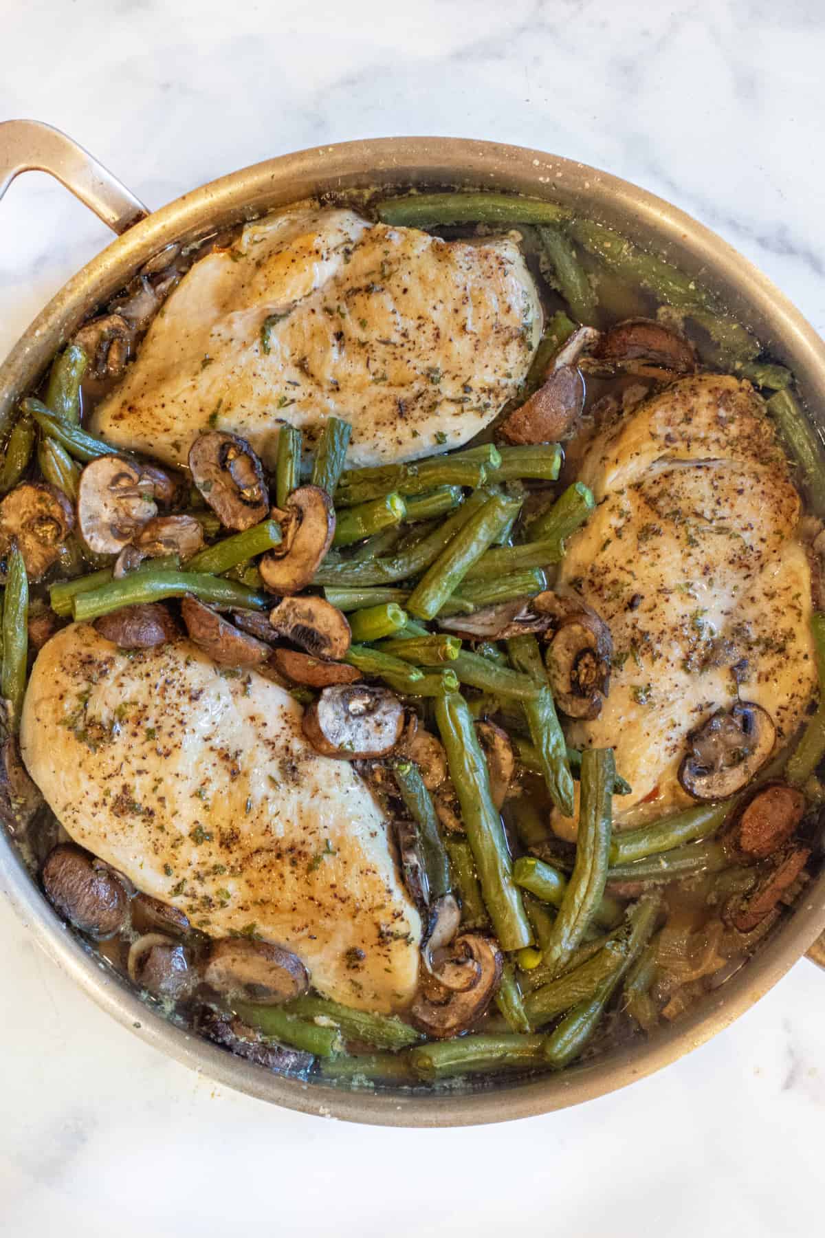 an overhead of a pan with cooked chicken breasts, green beans, and mushrooms.