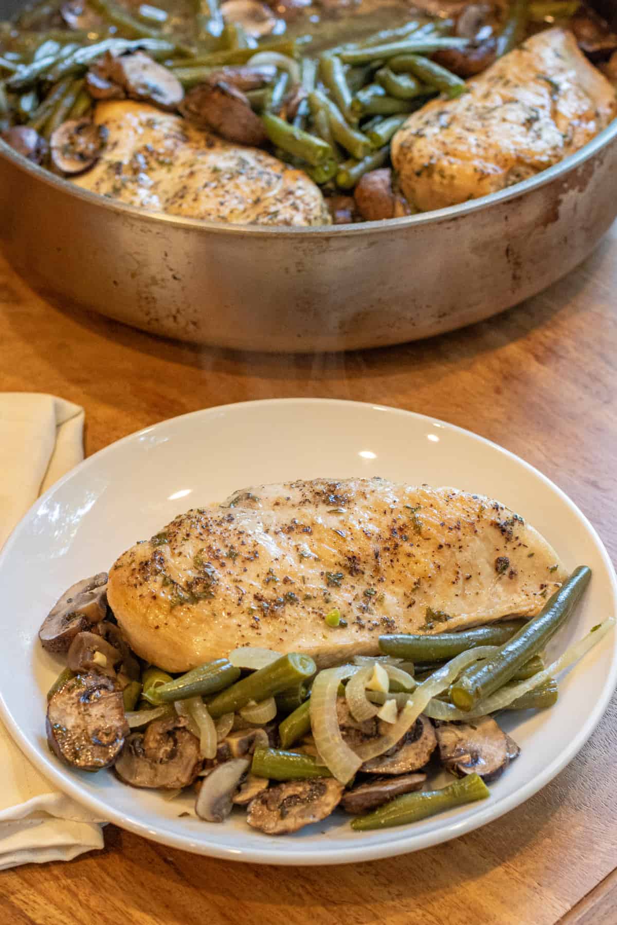 a plate with cooked chicken breast and green beans and mushrooms.