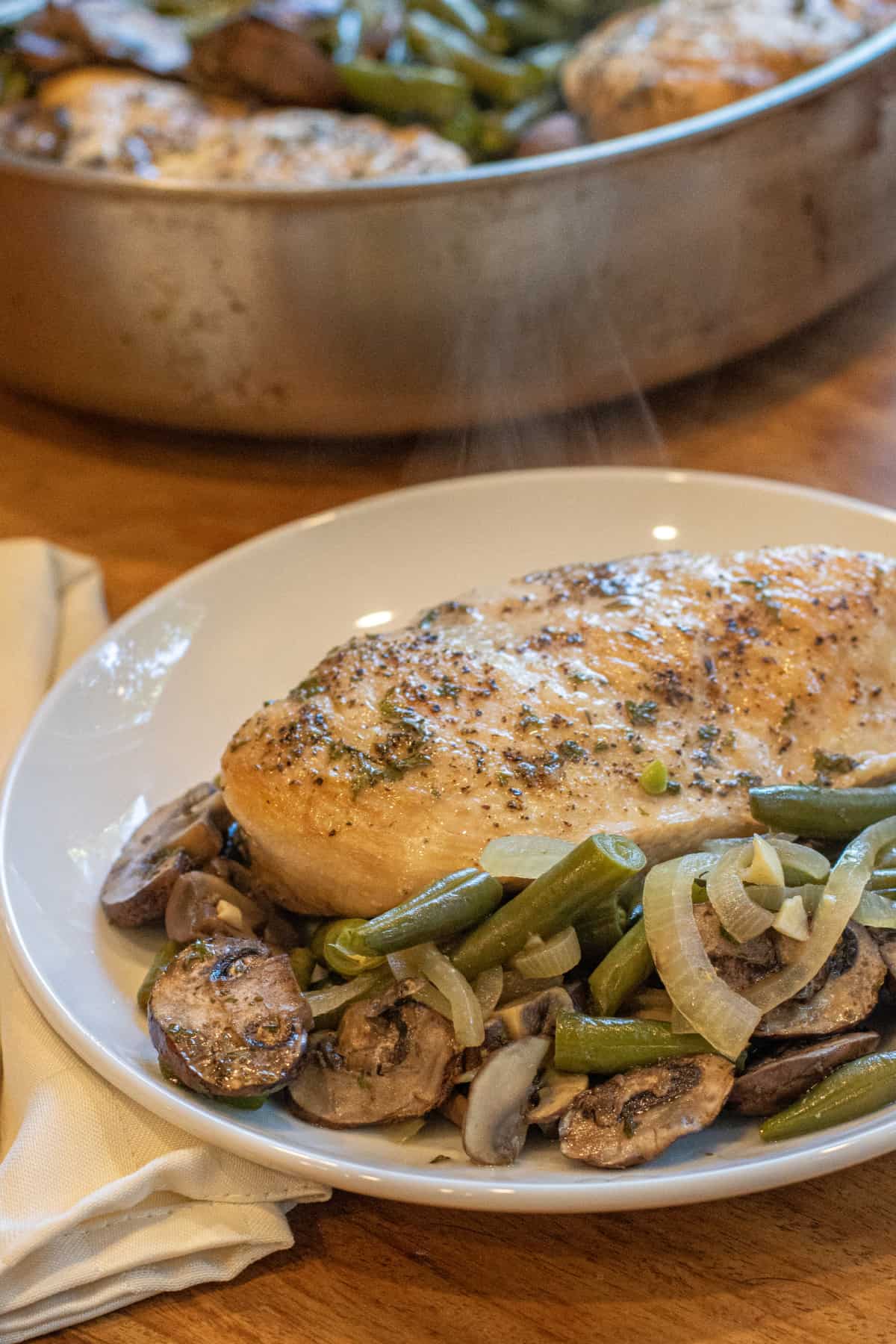 a plate with cooked chicken breast and green beans and mushrooms.