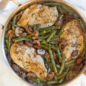 an overhead of a pan with cooked chicken breasts, green beans, and mushrooms.