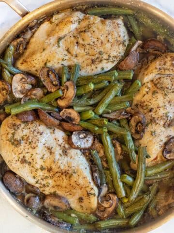 an overhead of a pan with cooked chicken breasts, green beans, and mushrooms.