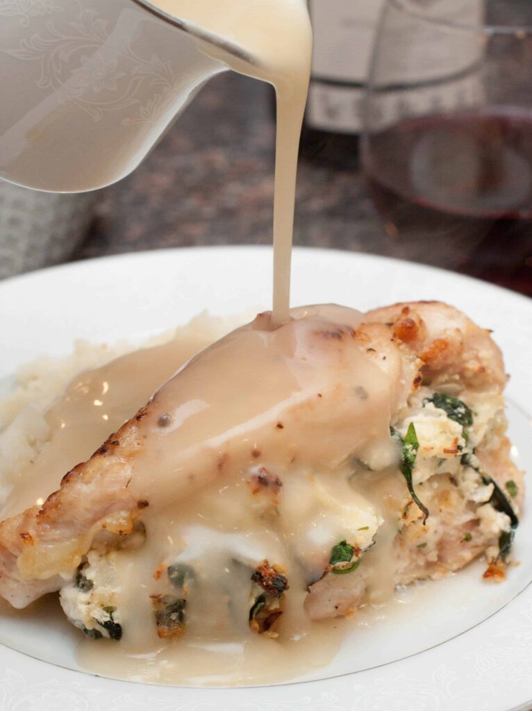 a plate with stuffed chicken with gravy being poured on it