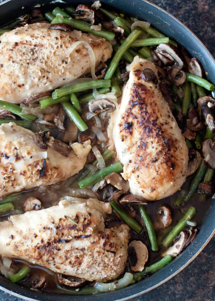 overhead of cooked chicken breasts with green beans and mushrooms in a skillet.