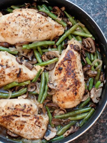 overhead of cooked chicken breasts with green beans and mushrooms in a skillet.