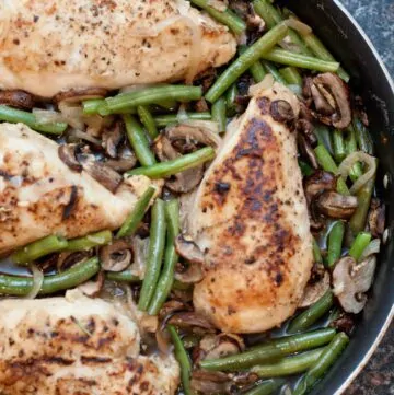 overhead of cooked chicken breasts with green beans and mushrooms in a skillet.