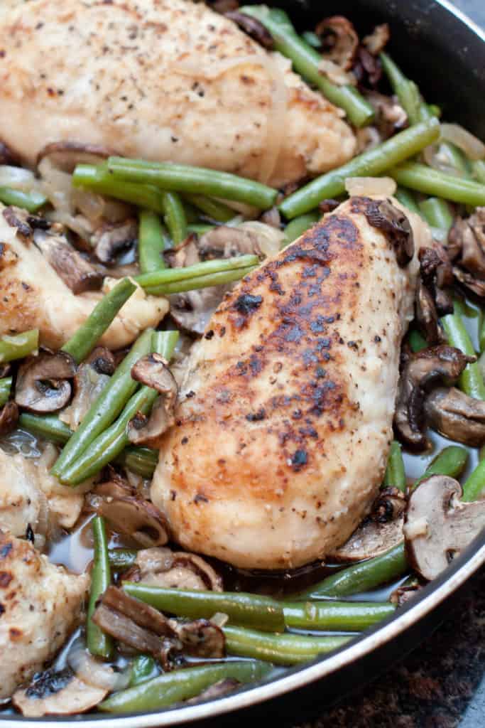 cooked chicken breasts with green beans and mushrooms in a skillet.