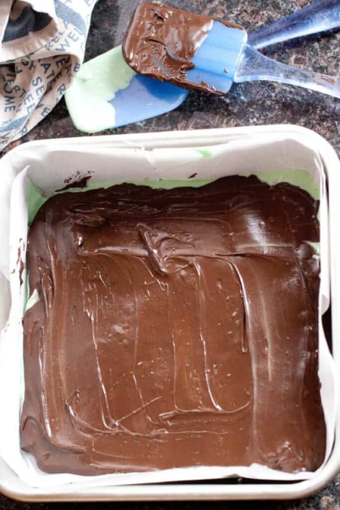 a square tray of cooled chocolate with spatulas behind it.
