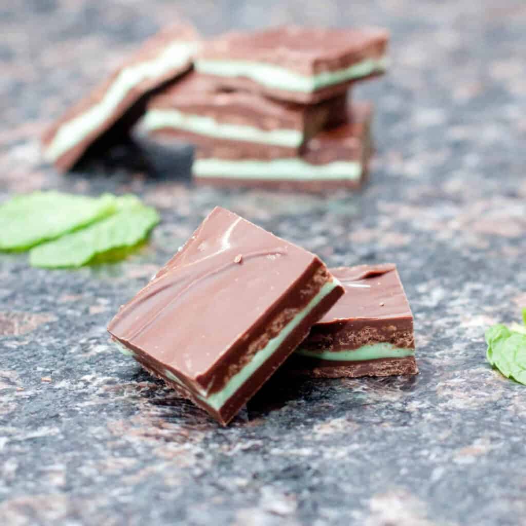 homemade square andes mints on a counter with mint leaves and a stack behind it.