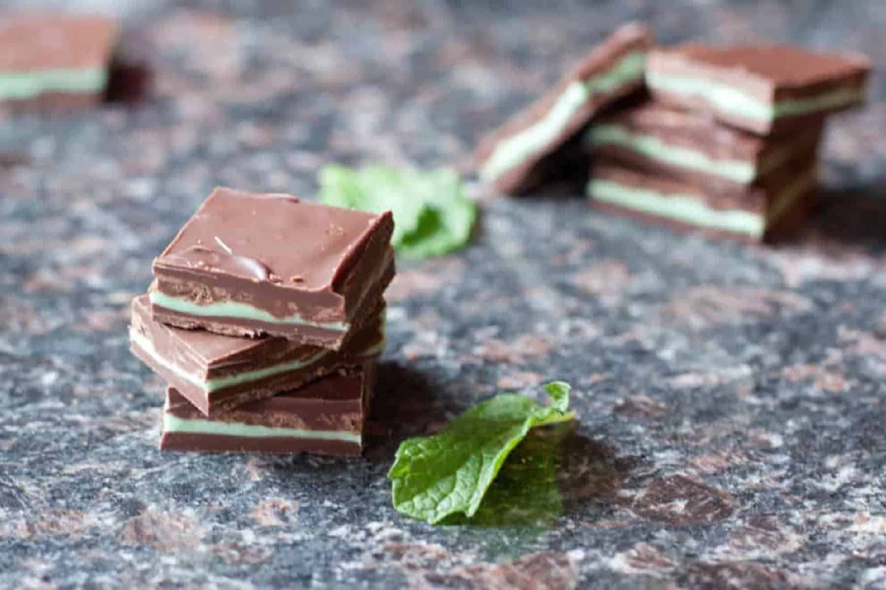 homemade square andes mints on a counter with mint leaves and a stack behind it.