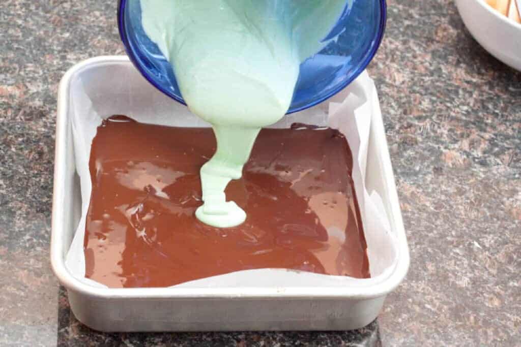 a square baking dish with melted chocolate in it and green colored chocolate being poured in over the chocolate.