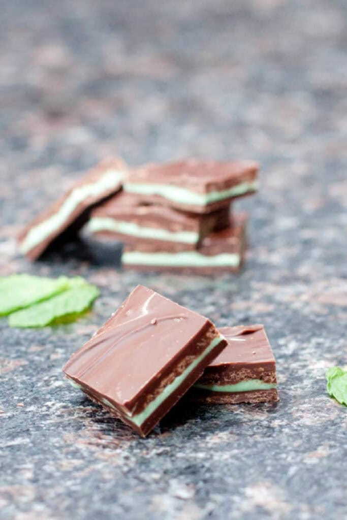 homemade square andes mints on a counter with mint leaves and a stack behind it.