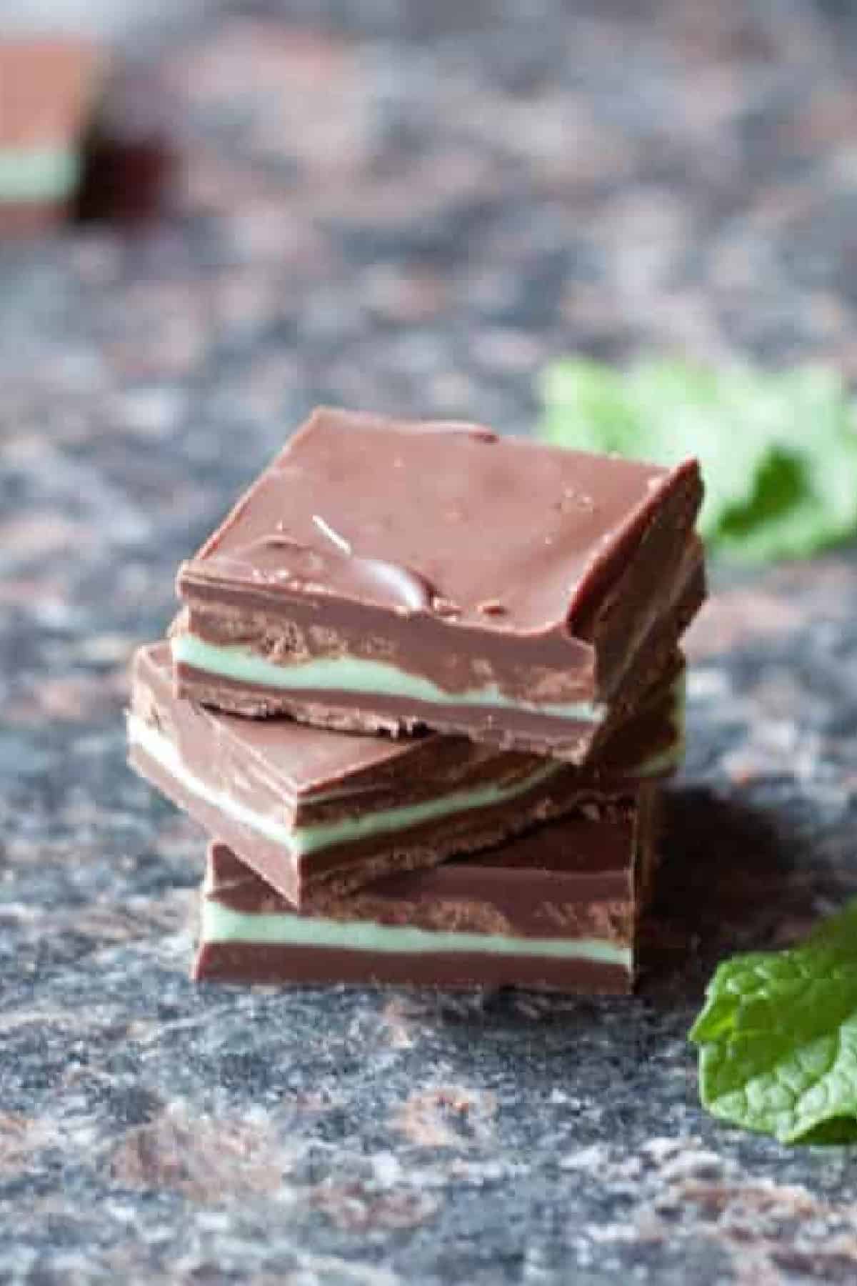homemade square andes mints on a counter with mint leaves and a stack behind it.