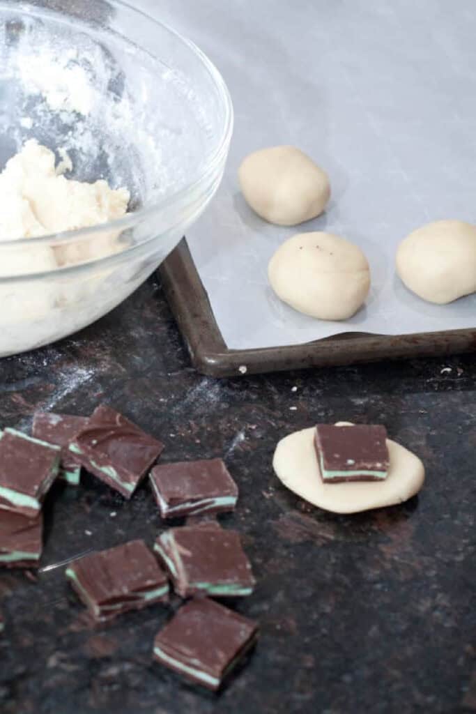 a bowl of dough and dough balls on parchment paper lined tray, homemade andes mints, and dough with a homemade andes mint in it.