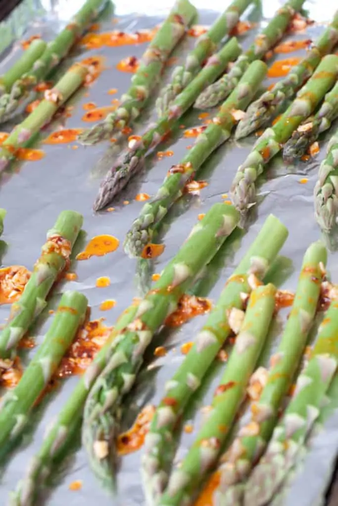 raw asparagus on foiled lined baking sheet with garlic oil drizzled on.