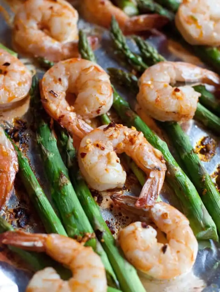 a close up of cooked shrimp and asparagus on a baking sheet.