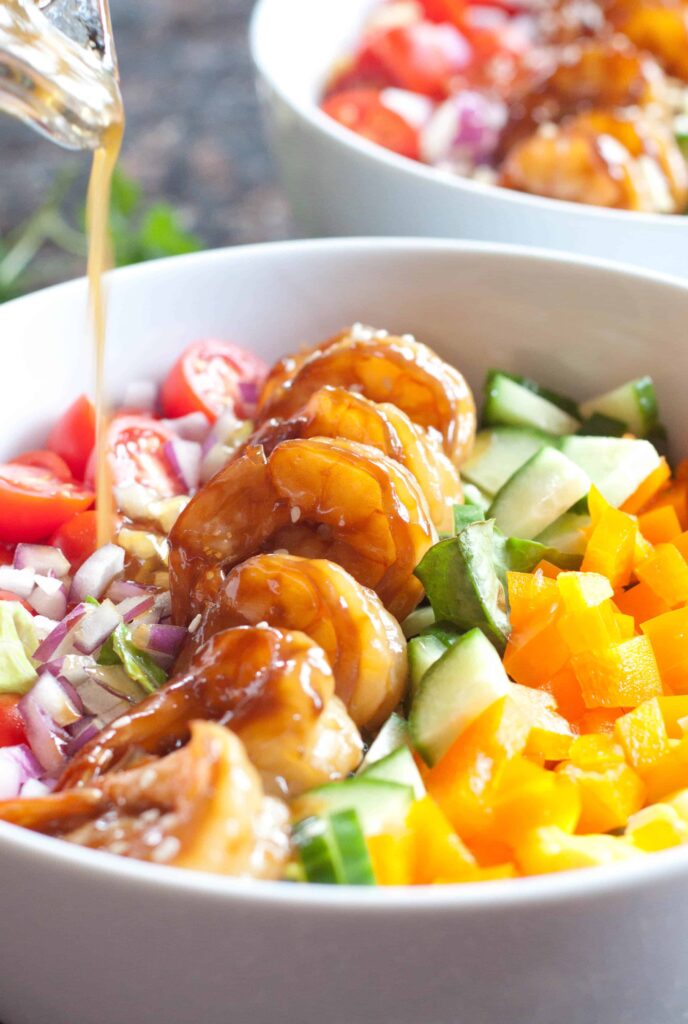teriyaki shrimp salad in a bowl with dressing poured on top.
