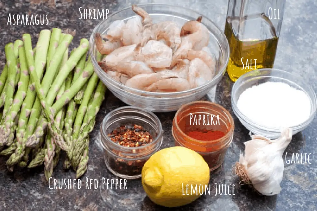 asparagus, shrimp, oil, red pepper, paprika, salt, garlic, and a lemon on a counter.