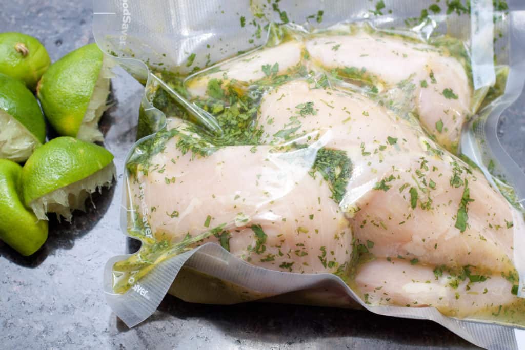 raw chicken marinating in vacuum sealed bag with juiced limes 